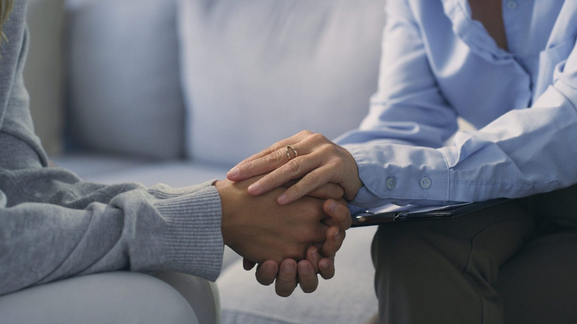 The Therapist gently holding client's hands on couch.